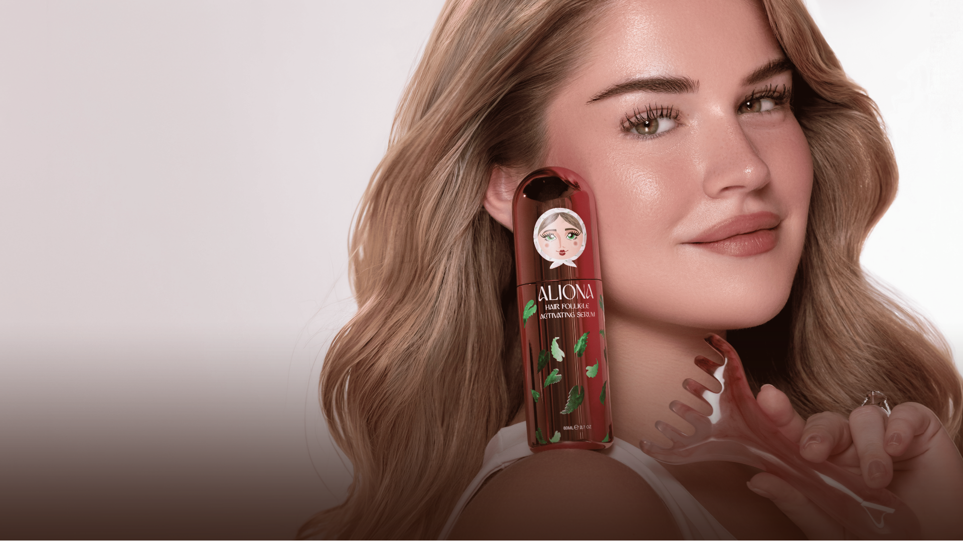 Woman holding a bottle of Aloma hair product with a neutral background